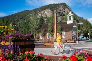 Frisco Main Street with flowers and woman walking bike in front of Schoolhouse Museum