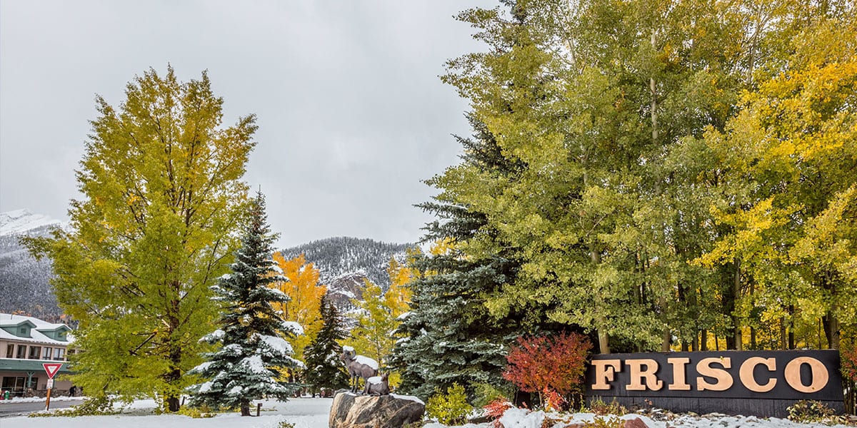 Frisco sign surrounded by trees with fall colors and snow covering the ground