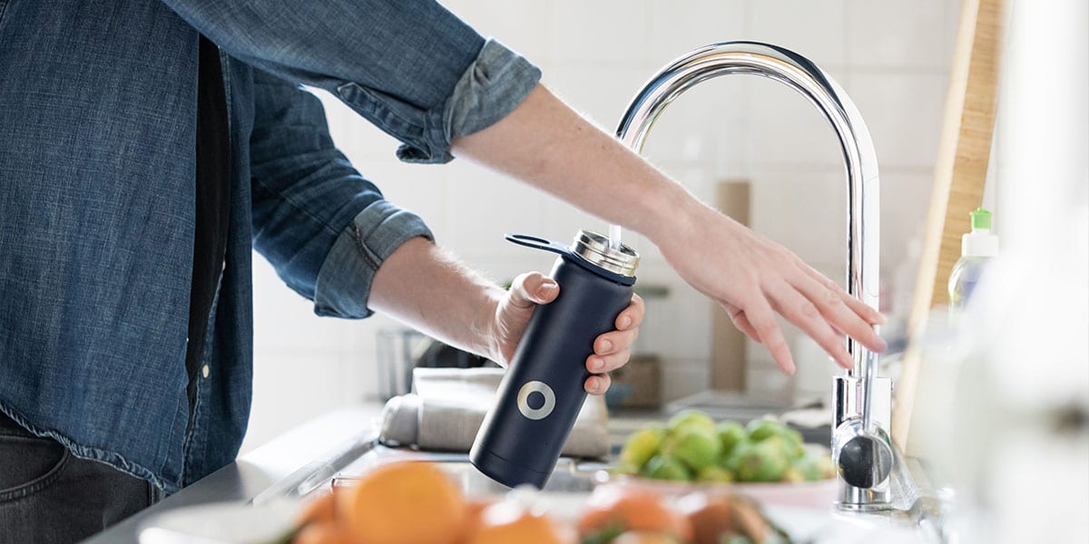 Closeup of person filling a water bottle at a kitchen faucet