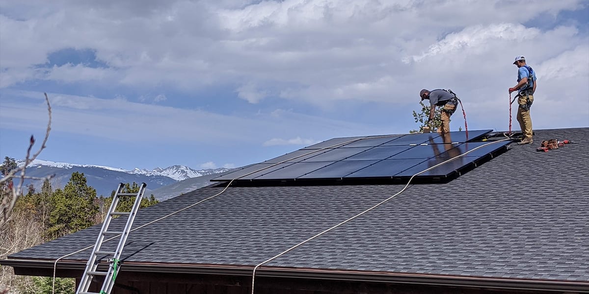 Two workers on rooftop installing solar panels.