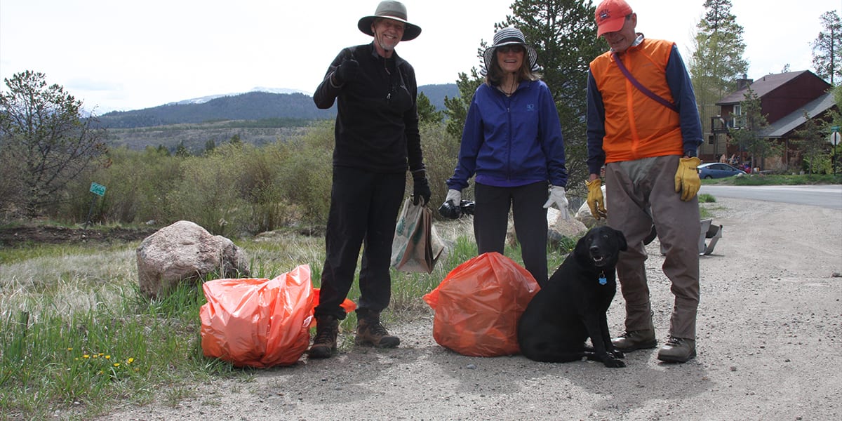 Three people with orange trash bags and a black dog.