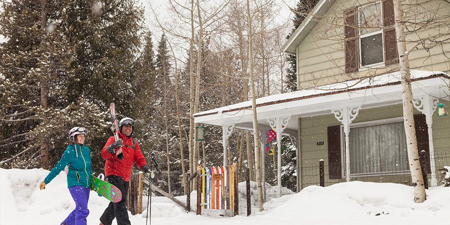 Skier and snowboarder in front of house