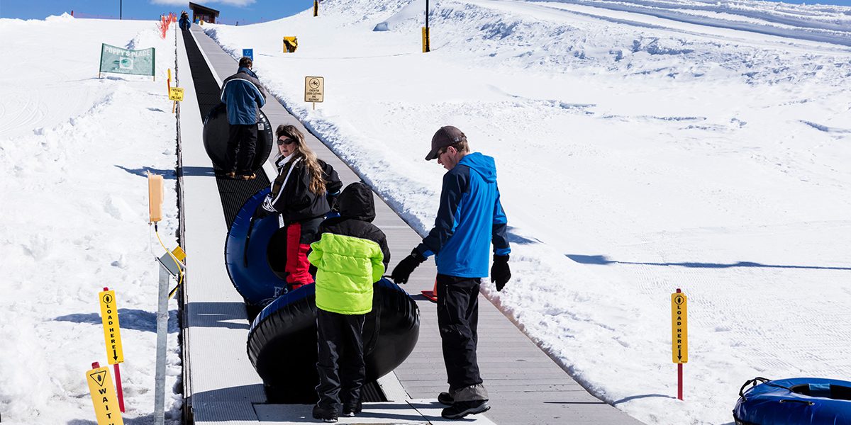 Tubing hill attendant helping person get on magic carpet at Frisco Adventure Park