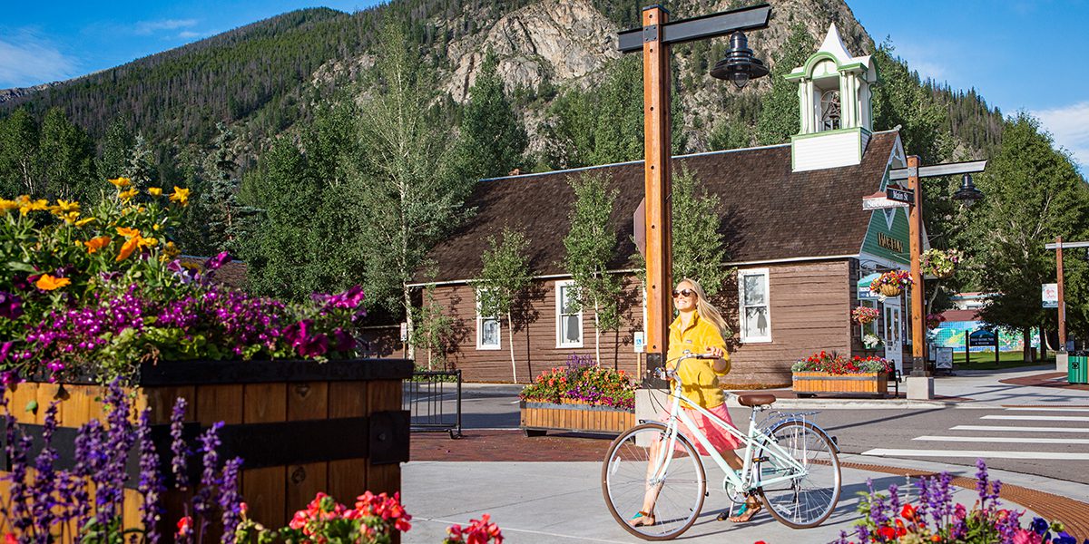 Woman pushing a bike down main street with the Frisco Historic Park & Museum on the background