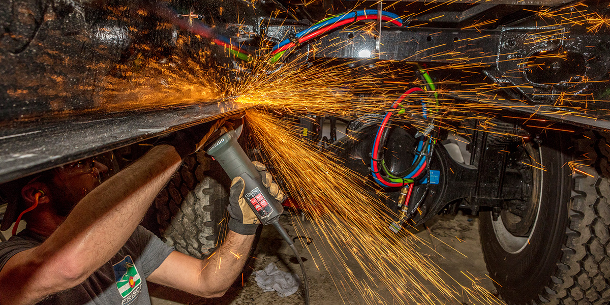 Fleet employee cutting metal with sparks flying under vehicle