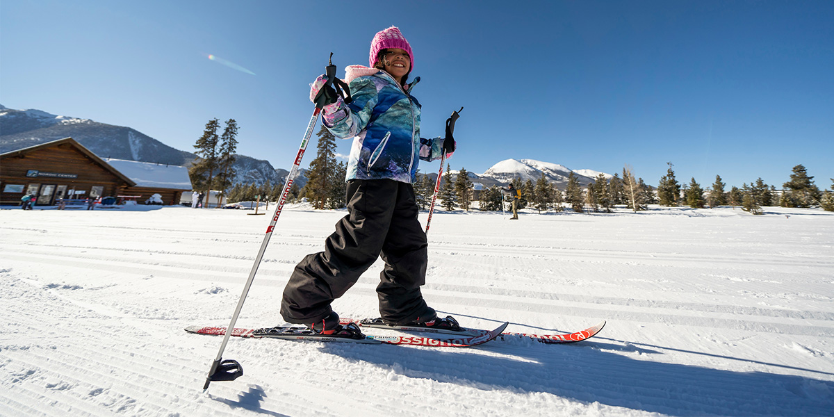 Girl on cross country skis on snow in front of the Frisco Nordic Center lodge